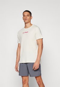 Ljusgrön kortärmad träningströja med en röd "TRAIL"-logotyp på bröstet, parat med grå shorts i ett lätt material.