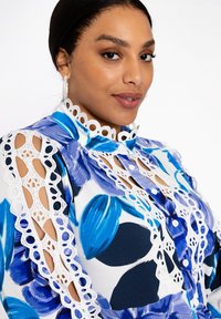 Bloemige blouse in blauw en witte stof met kantaccenten, hoge kraag, knoopsluiting en uitsnijdingen op de mouwen.