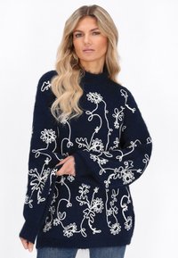 Marineblauwe gebreide trui met witte bloemenbroderie, oversized pasvorm, hoge nek en lange mouwen, met een fuzzy afwerking.