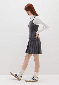 Vestido gris a rayas con un cuerpo ajustado y falda plisada, combinado con una blusa blanca de manga larga y zapatillas. Tejido texturizado, cintura definida.