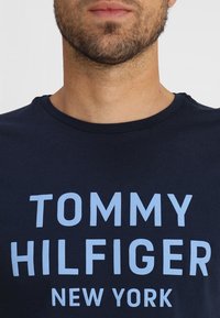Navy blue cotton T-shirt featuring light blue text that reads "TOMMY HILFIGER NEW YORK," with a crew neck and short sleeves.
