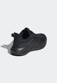 Černá sportovní bota s texturovaným pleteným svrškem, plochými tkaničkami, polstrovaným límcem a elegantní gumovou podešví s minimálním brandingem.