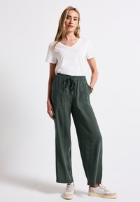 Letvægts hvid T-shirt med V-udskæring, parret med løstsiddende bukser i mørkegrøn med elastisk talje, der har to forlommer og tekstureret stof.