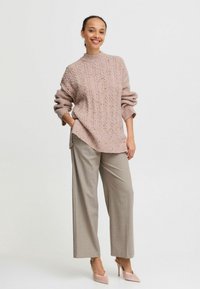 Cable-knit trui in zachtroze, hoge hals, ontspannen pasvorm. Gecombineerd met lichtgrijze, wijde broek en blush hakken. Minimalistische accessoires.