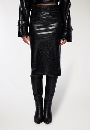Gonna a tubino nera a vita alta in finta pelle lucida, con texture morbida e design aderente, abbinata a stivali neri fino al ginocchio.