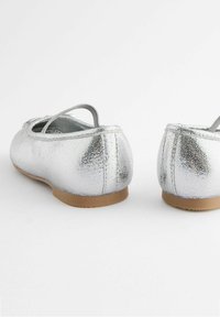 Ballerine metallizzate argento con superficie testurizzata, cinturino elastico e suola beige, caratterizzate da una punta arrotondata e un design semplice.