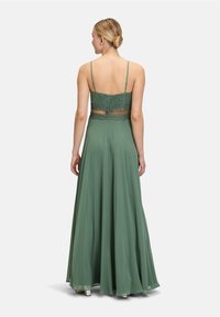 Długa zielona sukienka na cienkich ramiączkach, z koronkowymi detalami na plecach i zwiewnym, satynowym dołem. Cechuje się dopasowanym połowem i zapięciem na zamek.