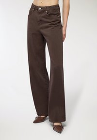 Brązowe dżinsy o szerokich nogawkach, wykonane z miękkiego denimu bawełnianego, z wysokim stanem, przednimi kieszeniami i subtelnymi detalami w przeszyciach.