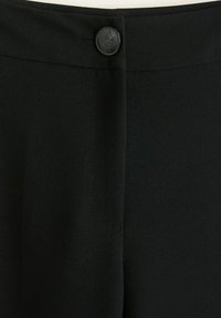 Czarne spodnie z materiału o gładkiej teksturze; mają zapięcie na guzik z przodu oraz delikatnie przeszyty szew biegnący wzdłuż środka.