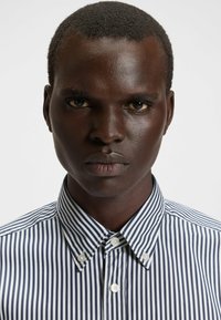 Marineblå og hvid stribet skjorte med krave, der kan knapres, fremstillet i letvægtsstof og med markante lodrette striber.