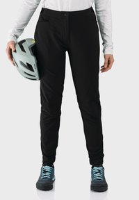 Schwarze Outdoor-Hosen mit schlanker Passform und zwei Fronttaschen. Das Modell hält einen hellblauen Helm und trägt blaue und schwarze Schuhe.