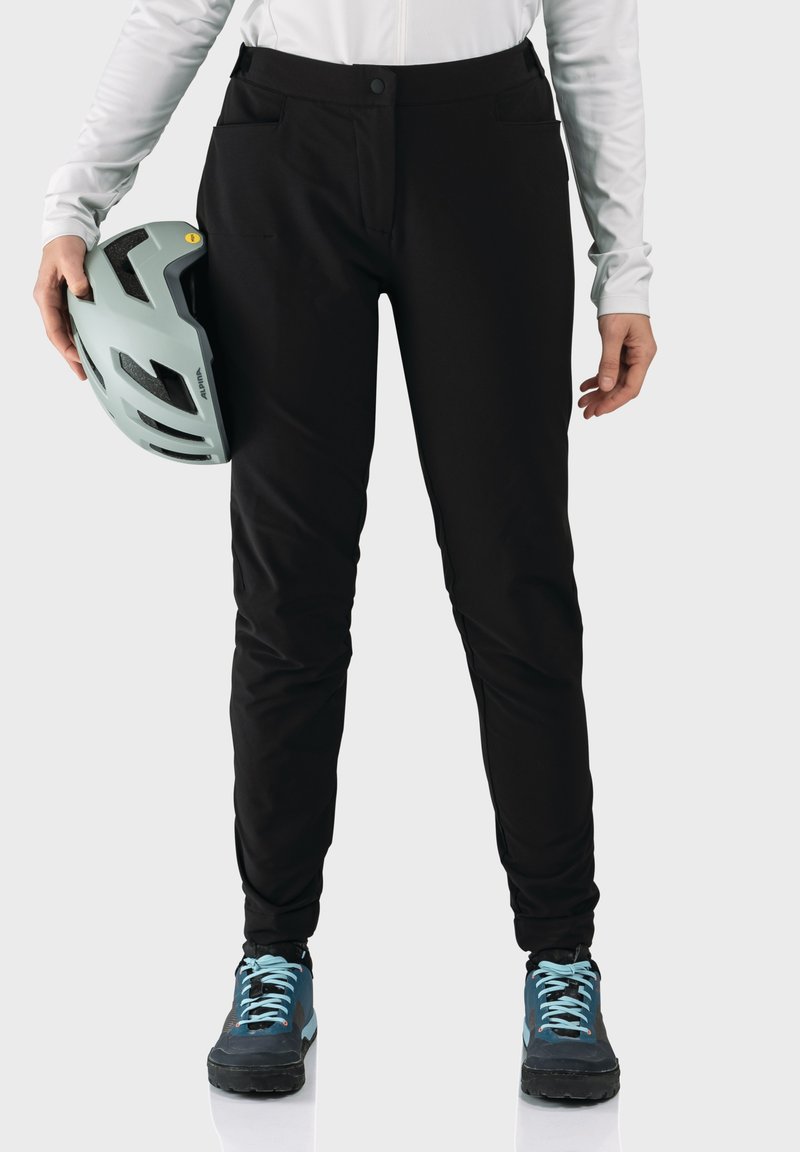 Schwarze Outdoor-Hosen mit schlanker Passform und zwei Fronttaschen. Das Modell hält einen hellblauen Helm und trägt blaue und schwarze Schuhe.