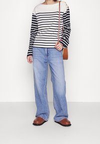 Gestreepte lange mouw top in crème en marineblauw, met accenten van gouden knopen. Gecombineerd met lichtblauwe wijdpijpen jeans en bruine instappers.