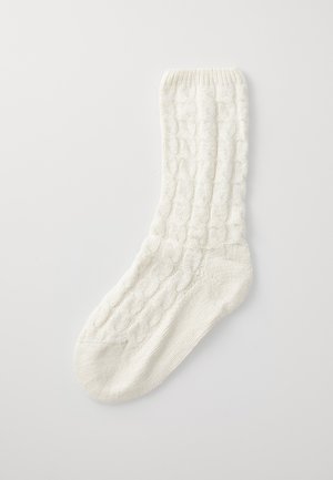 White knitted sock with a textured cable pattern and a ribbed cuff. Made from soft material, featuring a smooth toe and reinforced heel.
