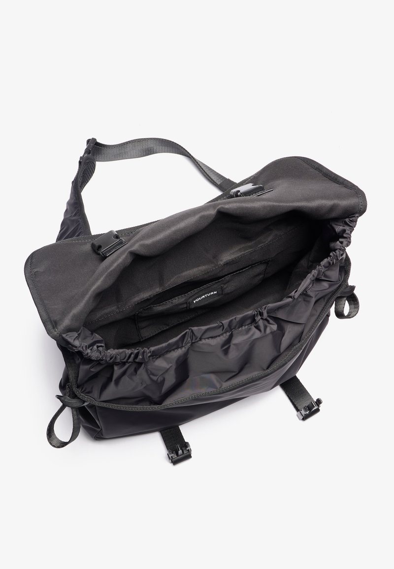 Bolso mensajero negro hecho de nylon suave, que presenta un cierre de cordón, correas ajustables y un interior espacioso con un bolsillo.