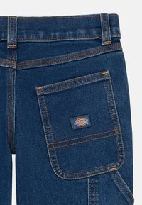 Dunkelblaue Denim-Jeans mit Gesäßtasche, die orangefarbenen Nähten und einem kleinen rechteckigen Dickies-Markenlabel.