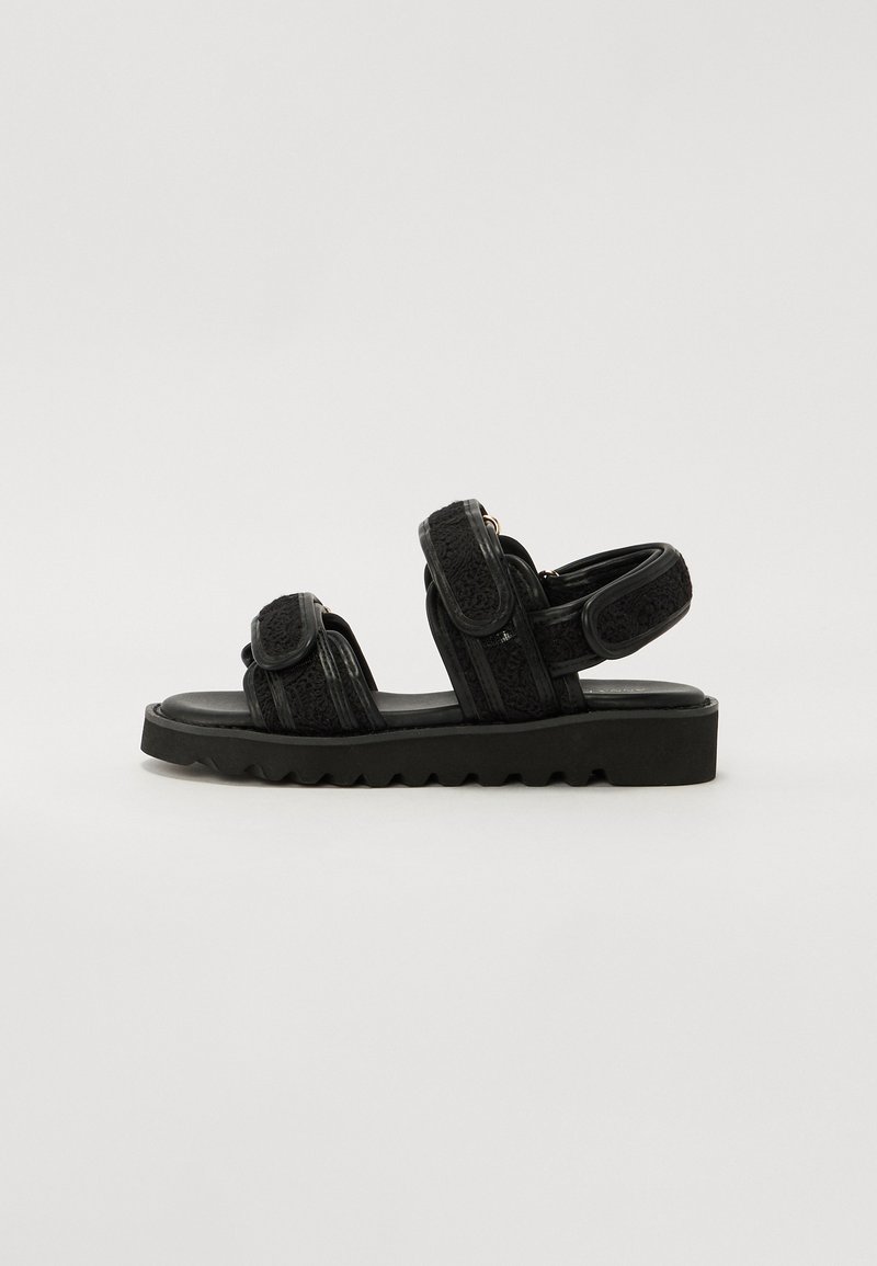 Sorte sandaler med tykke, teksturerte stropper og justerbare lukkinger. Har en kraftig, rugglete såle for godt fotfeste og komfort.