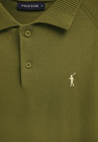 Zielona oliwkowa koszulka polo z prążkowanym kołnierzykiem, dwoma guzikami, małym białym haftowanym logo gracza polo i metką "Polo Club" w rozmiarze medium.