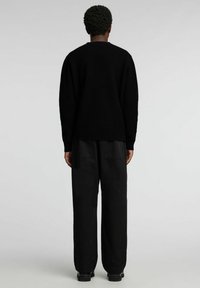 Schwarzer Pullover mit legerer Passform und Rundhalsausschnitt, aus strukturiertem Stoff, kombiniert mit lockeren schwarzen Hosen und robusten schwarzen Stiefeln.