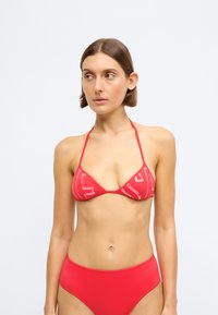 Κόκκινο μπικίνι τοπ με τριγωνικά cups, που διαθέτει λευκά γραφικά σχέδια. Το υλικό φαίνεται λείο και ελαστικό, με λεπτές τιράντες.