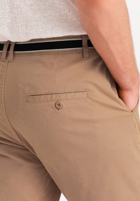 Pantaloni khaki realizzati in un tessuto morbido e leggero, con una tasca sul retro con chiusura a bottone e una cintura a strisce nere e grigie.