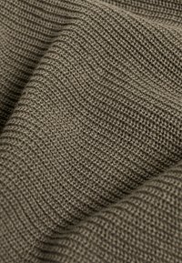 Strukturierter, olivgrüner Stoff mit einem gewebten Muster, das eine weiche, leicht dehnbare Oberfläche und subtile Variationen in der Tiefe zeigt.