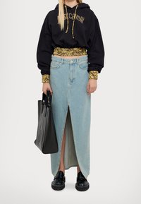 Persona che indossa un hoodie nero con dettagli animalier, una lunga gonna di jeans chiari con spacco frontale, scarpe con plateau nere e tiene una borsa a tracolla nera.