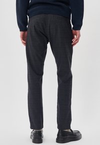 Pantaloni grigi scuri realizzati in tessuto strutturato, con una vestibilità slim e un delicato motivo a quadri, abbinati a scarpe nere.