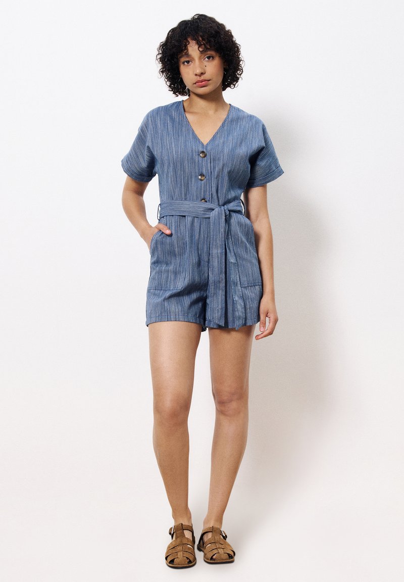 Jumpsuit court rayé bleu avec un décolleté en V, un devant boutonné, des manches courtes, une ceinture à nouer et deux poches avant.
