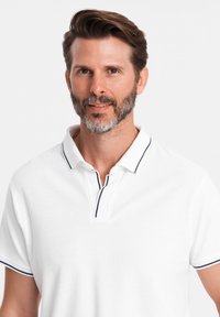 Vit polo t-shirt med krage, med kontrasterande marinblå trim vid kragen och ärmarna. Mjuk textur, korta ärmar och avslappnad passform.