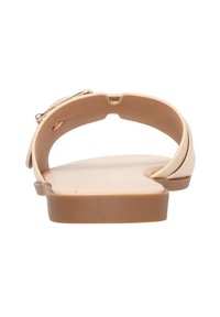 Sandali piatti beige con una soletta sagomata, due cinturini che si incrociano sulla parte superiore e un dettaglio in tonalità oro sulla parte superiore.