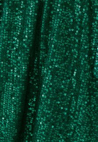 Roheline kangas, kaetud läikivate ümmarguste säbrudega, luues tekstureeritud pinna, millel on särav efekt. Üldine elav ja peegeldav välimus.