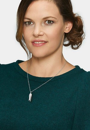Silbernes Necklace mit einem Feder-Anhänger, getragen über einem türkisfarbenen, strukturierten Pullover mit einem Bootsausschnitt und Puffärmeln.