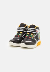Zapatillas negras de caña alta con acentos amarillos, cordones blancos y de colores, con un diseño de Super Mario y suela de goma texturizada.