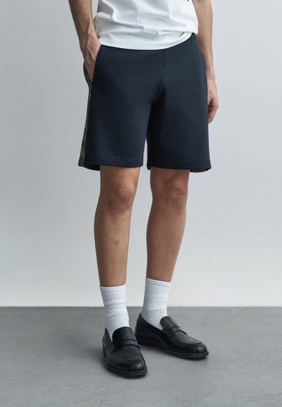 Shorts bleu foncé en tissu doux, avec un design texturé sur les côtés, longueur légèrement au-dessus du genou, dotés de poches et d'une taille élastique.