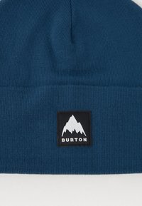 Niebieska dzianinowa czapka beanie z czarną metką przedstawiającą grafikę góry oraz napisem "BURTON". Gładka tekstura i dopasowany krój.