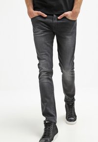 Slim-fit grå denimjeans med en lätt tvätt, fem fickor, bälteöglor och en mjuk textur, kombinerat med svarta högtopps-sneakers.