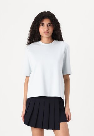 Light blue short-sleeve T-shirt with a round neck, featuring a relaxed fit. Paired with a pleated navy skirt, emphasizing texture and shape.