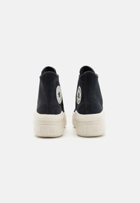Zapatillas altas de ante negro con una suela de goma crema, que presentan un parche de logo circular en cada lado y un acabado texturizado.