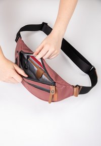 Compact roze heupzak met een gestructureerde buitenkant, ritssluitingen en bruine leren accenten. Verstelbare zwarte riem voor een veilige draagervaring.