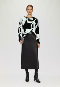 Zwarte en mintgroene gebloemde gebreide trui gecombineerd met een gladde zwarte satijnen midi-rok, aangevuld met zwarte enkellaarzen en een zilveren clutch.