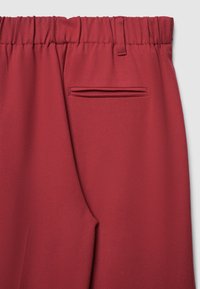 Pantaloni sportivi color bordeaux con una fascia elastica in vita, caratterizzati da un tessuto elegante e testurizzato e una tasca posteriore discreta con una fessura orizzontale.