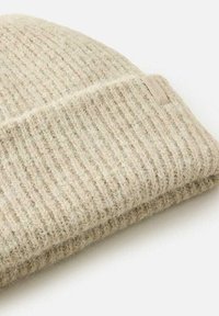 Beige strikket beanie med ribbet tekstur, lavet af blød uld. Har en foldet manchet og et lille, diskret mærke på siden.