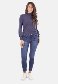 Maglione blu navy a maniche lunghe con colletto alto, abbinato a jeans blu attillati e sneakers bianche; presenta una texture morbida e una vestibilità casual.