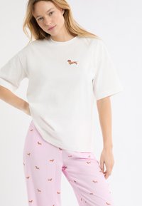 Maglietta bianca di cotone a maniche corte con un piccolo ricamo di un bassotto marrone sul petto, abbinata a pantaloni rosa a righe con stampe di bassotti.