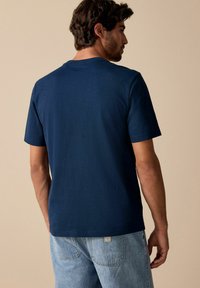 Camiseta de manga corta azul marino con cuello redondo, hecha de una tela suave. La vista trasera muestra una textura lisa y detalles de costura sutiles.