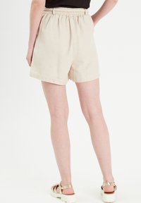 Shorts en coton beige avec une taille élastique, des poches latérales et une coupe décontractée. Convient pour une tenue décontractée par temps chaud.
