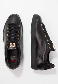 Svarta lädersneakers med gyllene öglor, texturerade detaljer och en slät yta. Har en dekorativ logotyp och en vadderad sula.