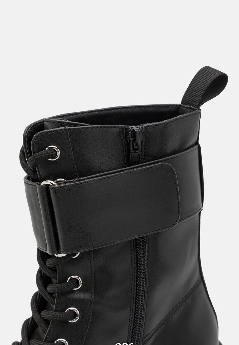 Schwarze Knöchelstiefel aus glattem Material, mit einem Reißverschluss, Schnürung an der Vorderseite und einem gepolsterten Schaft mit einem Klettverschluss.