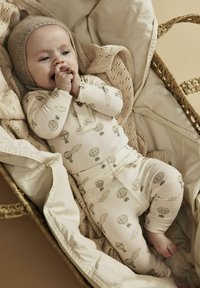 Pigiama in cotone leggero color crema con una texture a costine, caratterizzato da una stampa di palloncini giocosa. Il bambino è in un cesto intrecciato foderato con una coperta lavorata a maglia.